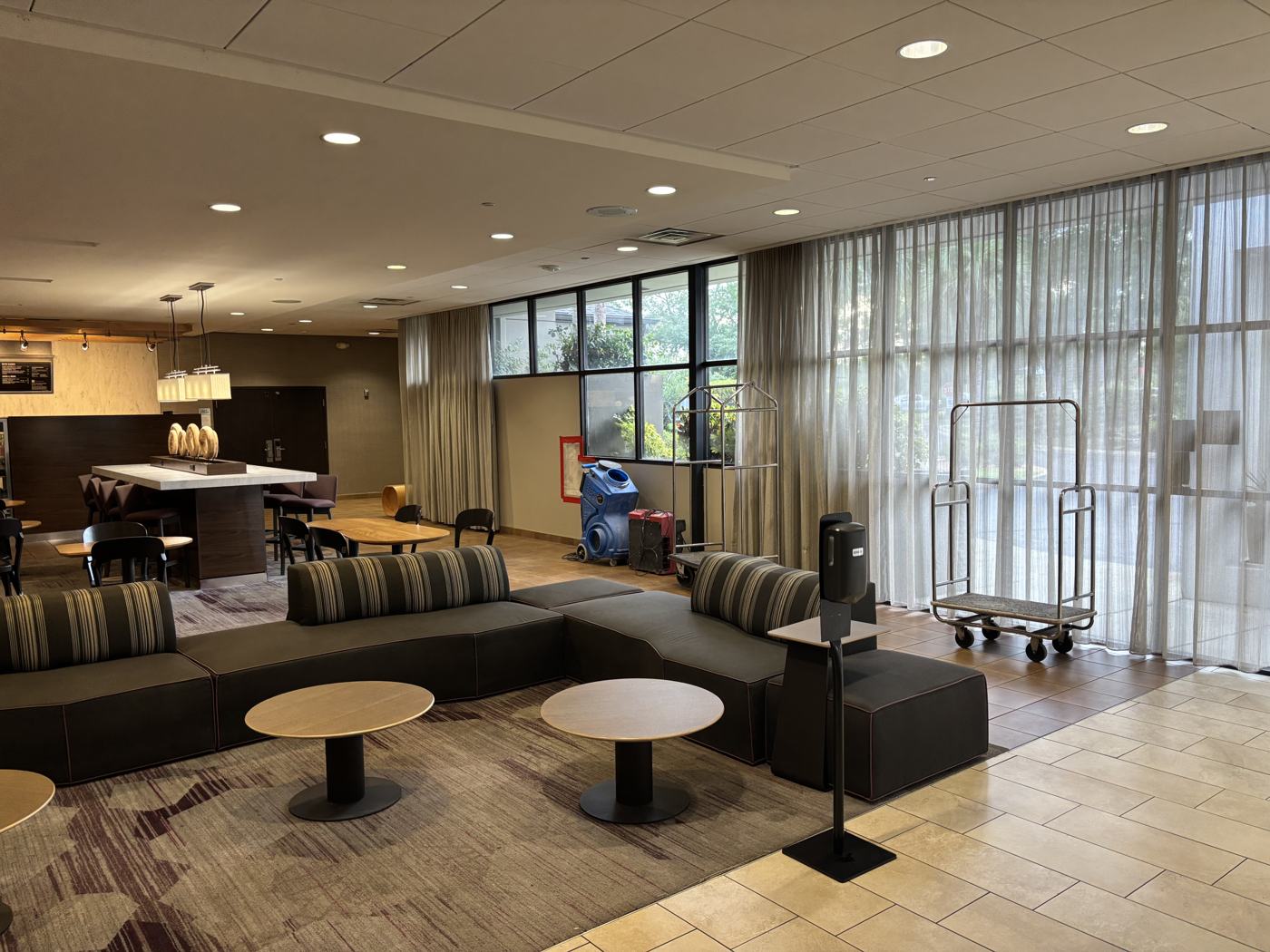 Hotel lobby open to guests during renovation, luggage carts staged and seating in use, with air scrubbers tucked against the wall.