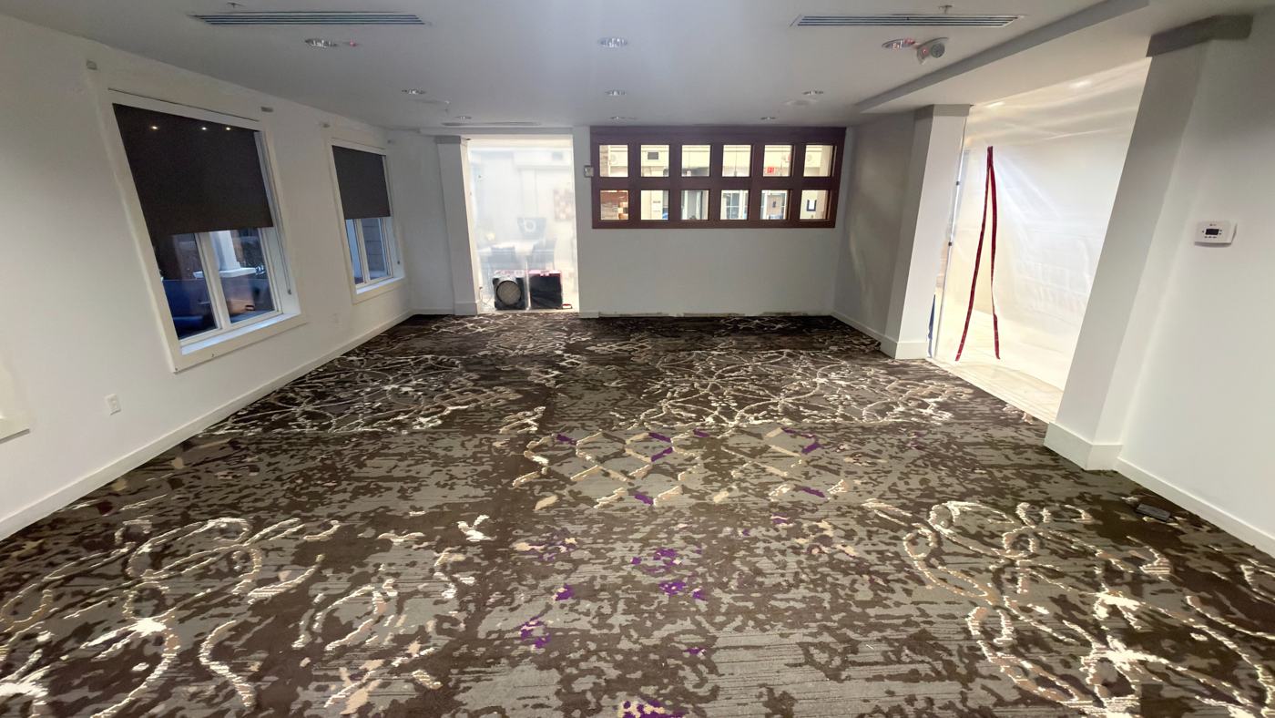 The same meeting room with new patterned carpet installed, walls finished, containment still sealing the doorway.