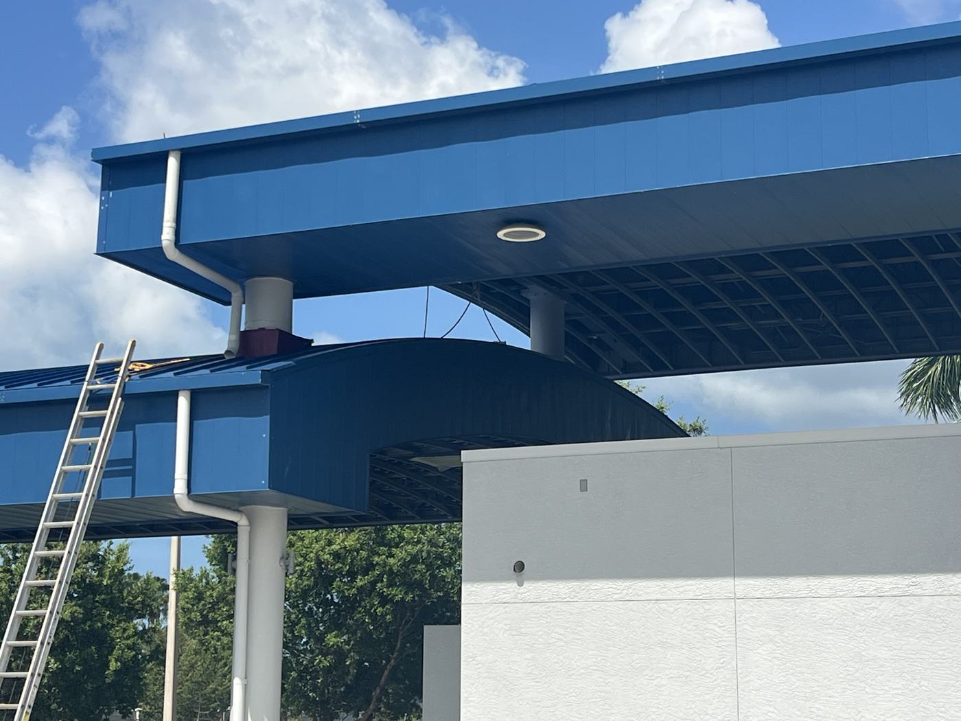 New blue standing-seam canopy roof, fascia, and downspout against fresh stucco.