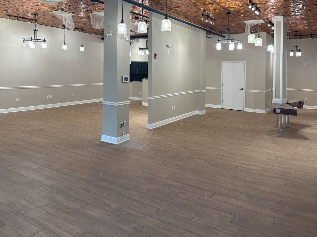 Wide view of the finished salon interior: wood-look tile, chair rail, pendant clusters, and new cabinetry ready for fit-out.